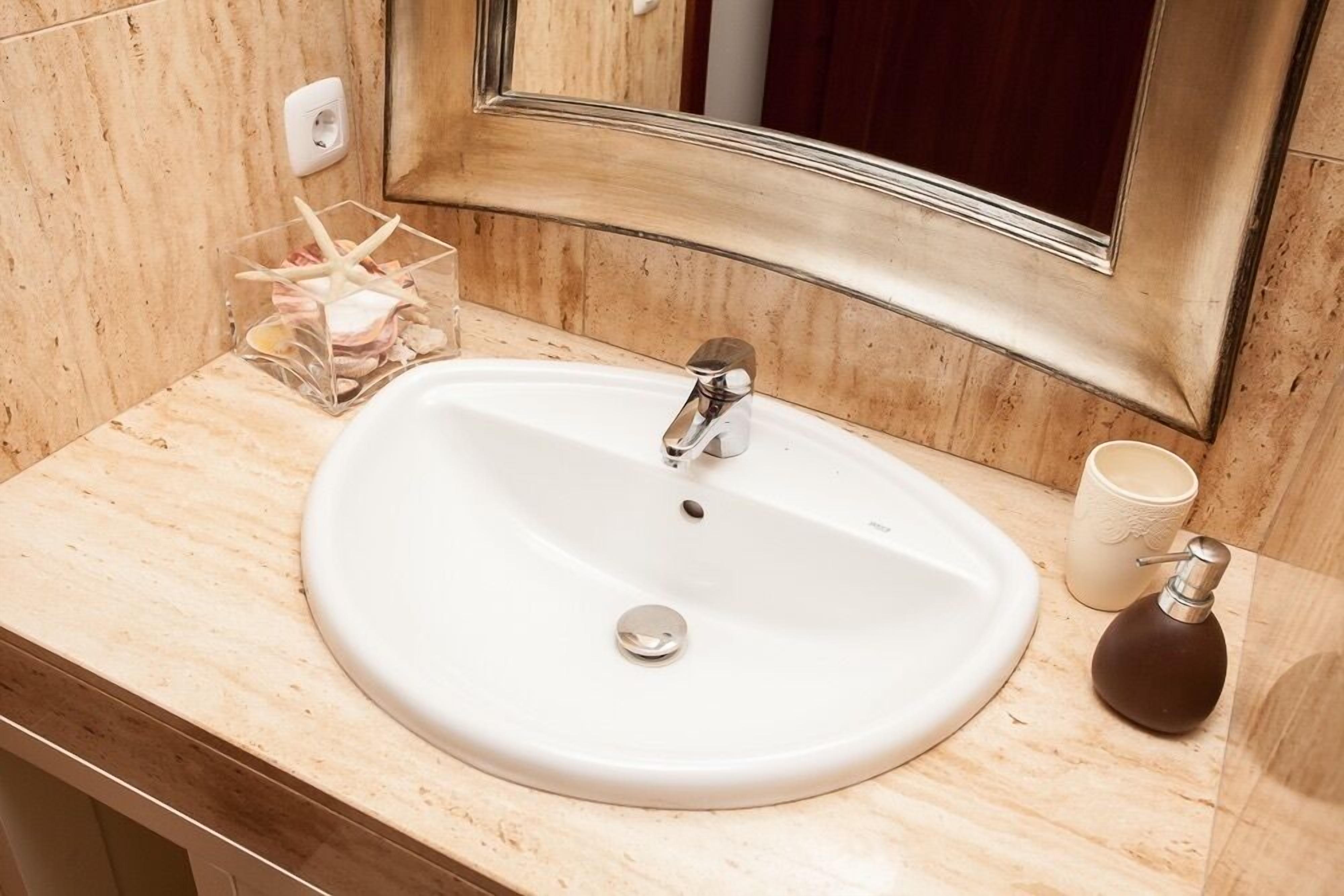 Un baño con lavamanos blanco, espejo y encimera color beige.