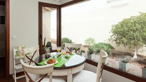 A dining area with a round table, white chairs, and a view of the garden through a large window.