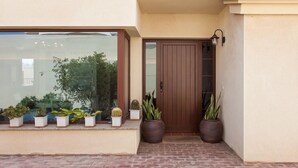 A building entrance with a brown door, potted plants, and a window with a view of greenery.
