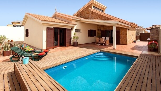 A modern house with a swimming pool, wooden deck, and outdoor furniture.