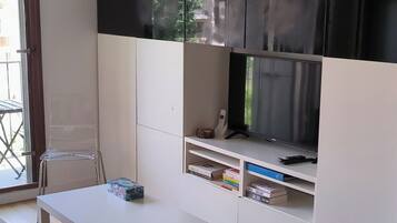 Un salon moderne avec une table blanche, un téléviseur posé sur un meuble et une bibliothèque.