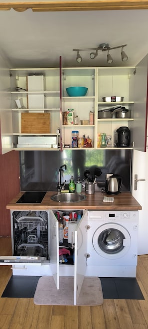A compact kitchen with a built-in washing machine, a sink, and a variety of kitchen utensils and appliances.
