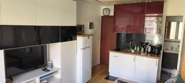 Una cucina compatta con mobili bianchi, un frigorifero nero, un forno a microonde e una macchina da caffè.