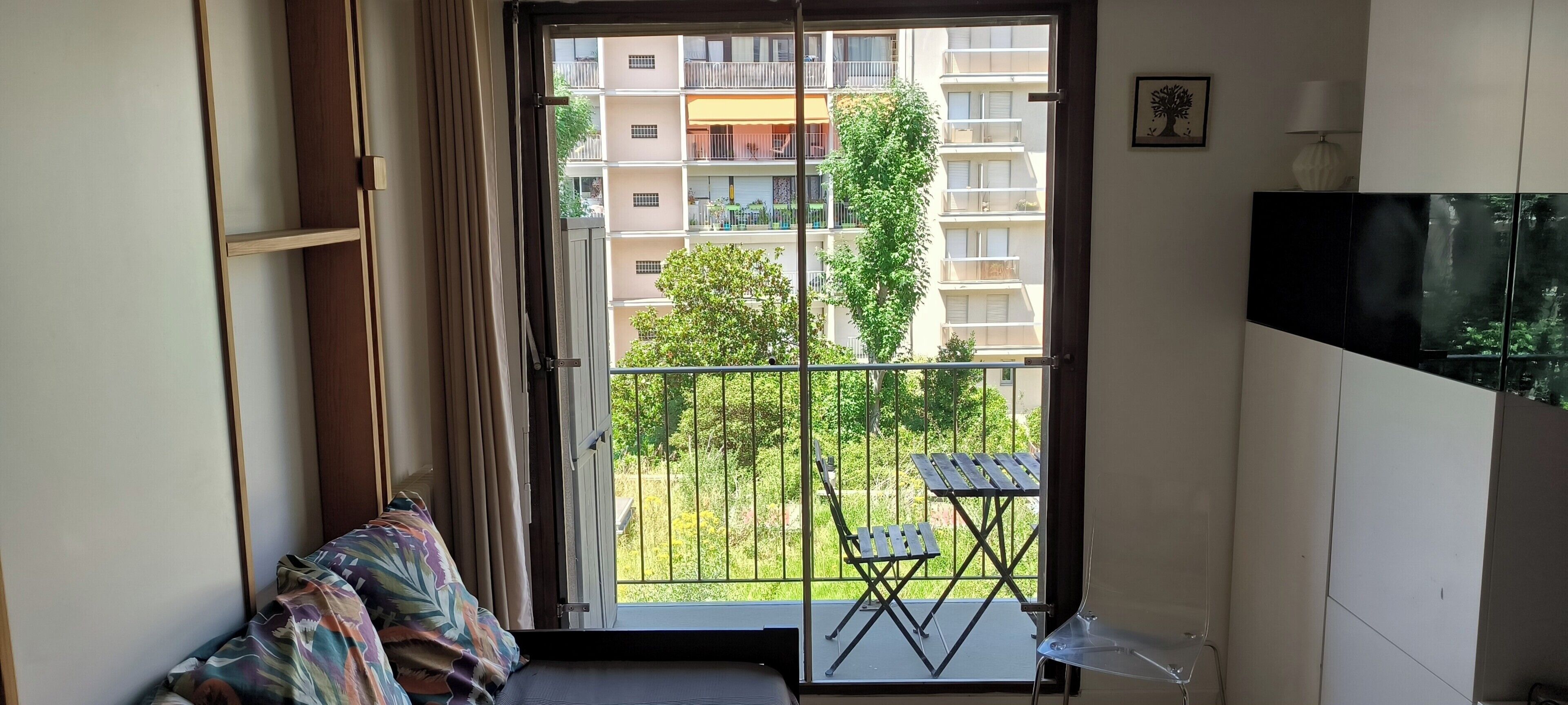 A balcony with a view of a residential building, a small table, and a chair.
