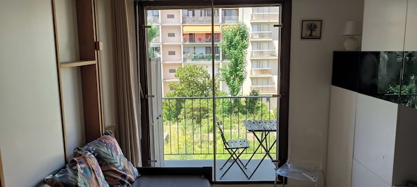A balcony with a view of a residential building, a small table, and a chair.