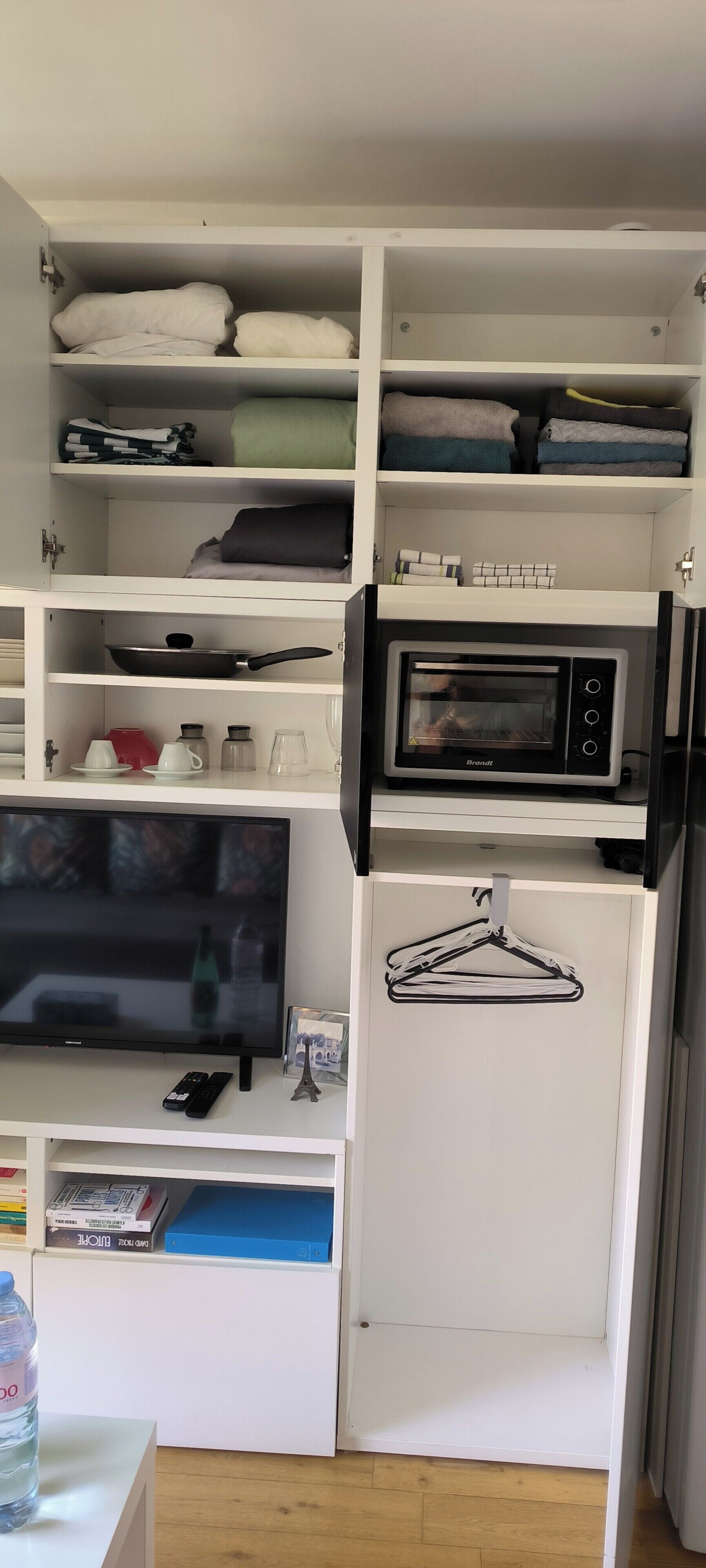 A compact kitchen with a microwave, a television, and a water bottle on the counter.