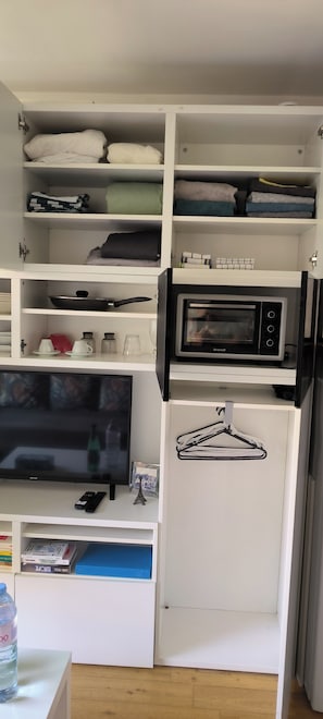 A compact kitchen with a microwave, a television, and a water bottle on the counter.