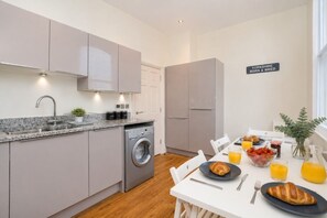 A modern kitchen with grey cabinets, a built-in washing machine, and a breakfast setup with croissants, fruit, and juice.