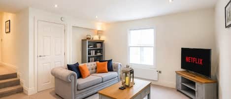 A living room with a sofa, coffee table, bookshelf, TV, and a door.