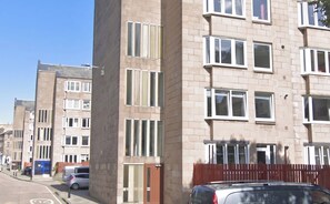 Un edificio residencial de varios pisos con fachada de ladrillo, múltiples ventanas y una entrada visible.