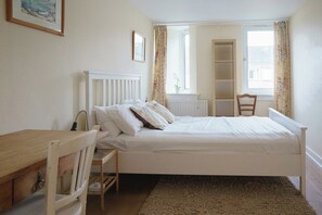 Un dormitorio con una cama individual, una silla de madera, un escritorio y un radiador.
