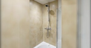 Un baño con azulejos color beige, una ducha con cabezal de ducha manual y una bañera.