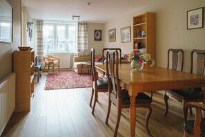 A dining area with a wooden table, chairs, a bookshelf, and a window with curtains.