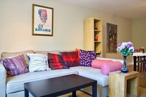 A living room with a sofa, a coffee table, a bookshelf, and a dining table with a vase of flowers.