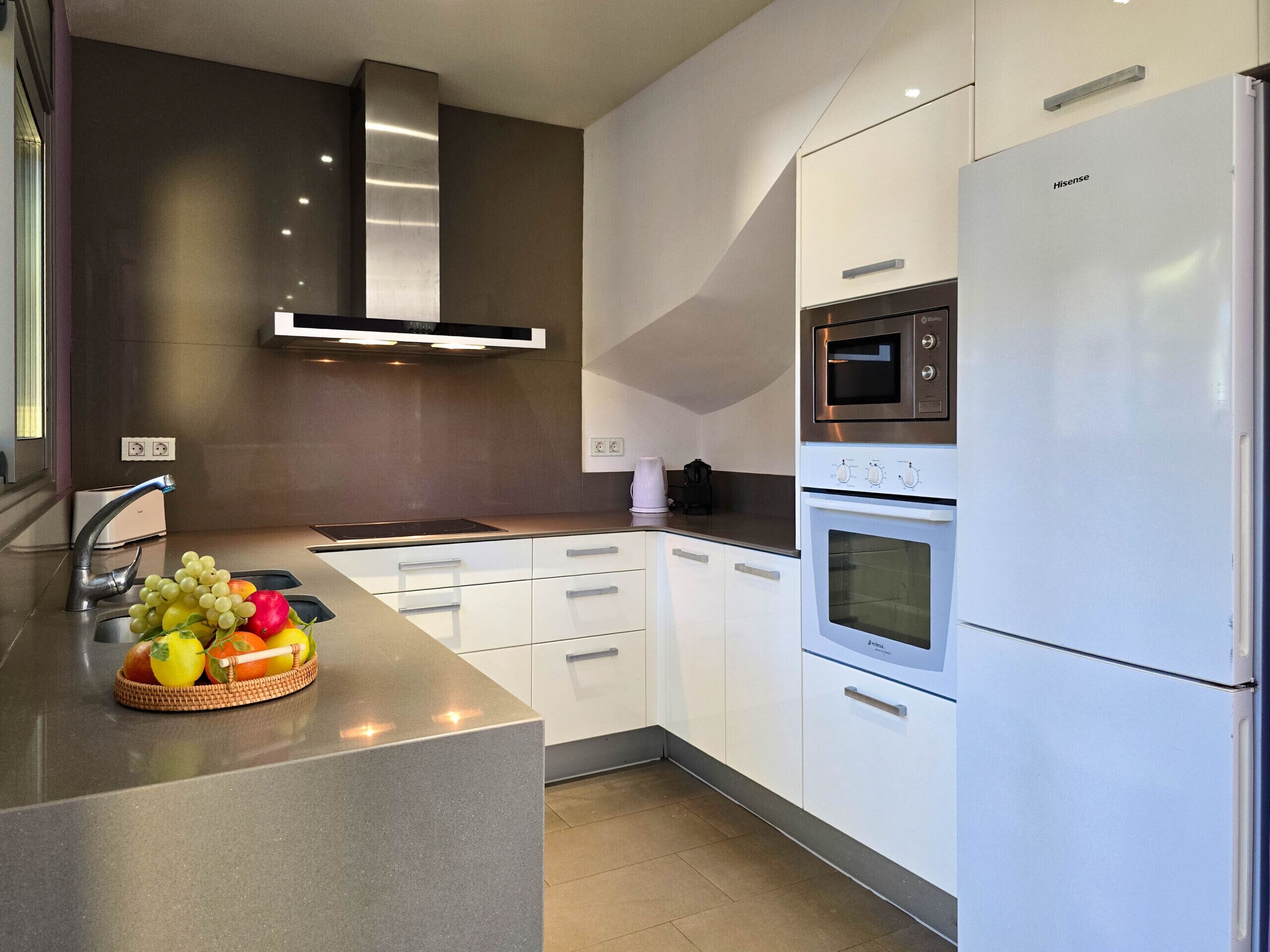 A modern kitchen with white cabinetry, a stainless steel range hood, a built-in oven, and a refrigerator.