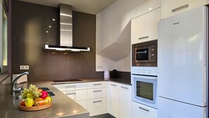 Une cuisine moderne avec des meubles blancs, une hotte en acier inoxydable, un four encastré et un réfrigérateur.