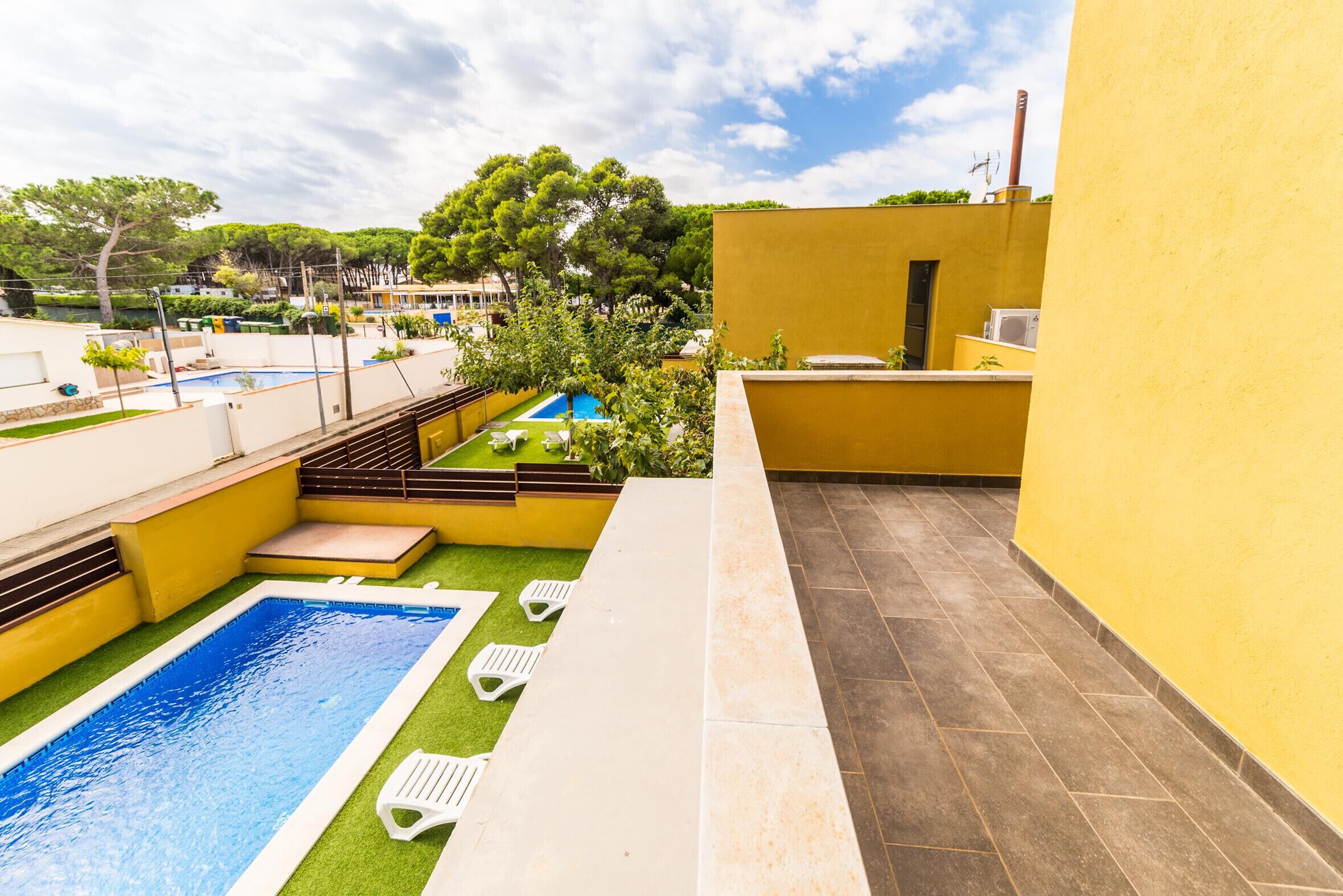 Un área de piscina en la azotea con una piscina pequeña, sillas de descanso y un edificio amarillo.
