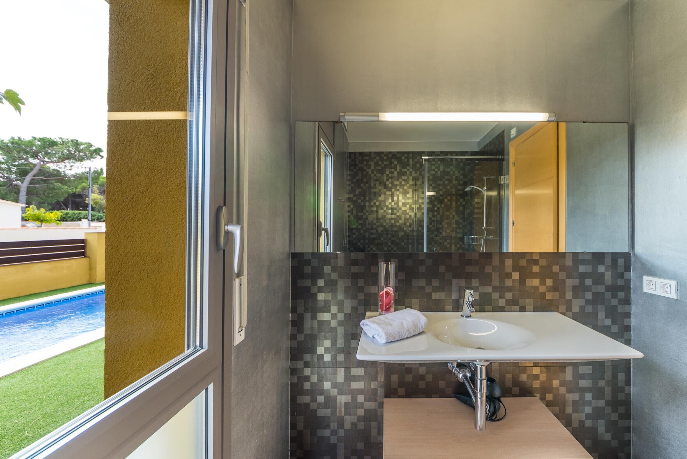Een moderne badkamer met een groot raam, een witte wastafel en een betegelde spatwand.