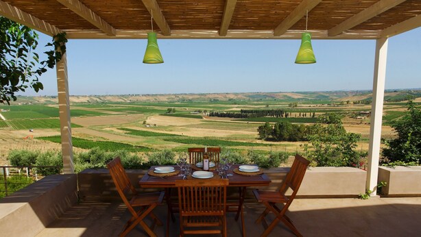 Une terrasse extérieure avec une table en bois dressée pour le repas, offrant une vue sur un paysage pittoresque.