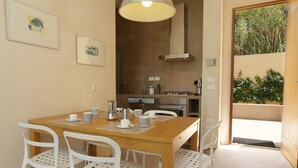 Un coin repas avec une table en bois et des chaises blanches, une cuisine en arrière-plan et des œuvres d’art encadrées accrochées au mur.