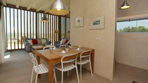 Un coin repas avec une table en bois et des chaises blanches, des œuvres d’art encadrées au mur et une vue dégagée grâce à de grandes fenêtres.