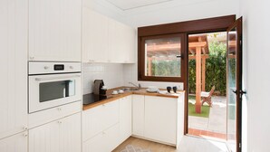 Une cuisine moderne avec des meubles blancs, un plan de travail en bois et une vue sur le jardin grâce à une porte vitrée.