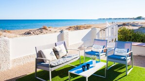 Une terrasse en bord de mer, dotée de mobilier d’extérieur, d’une clôture blanche et offrant une vue sur l’océan.