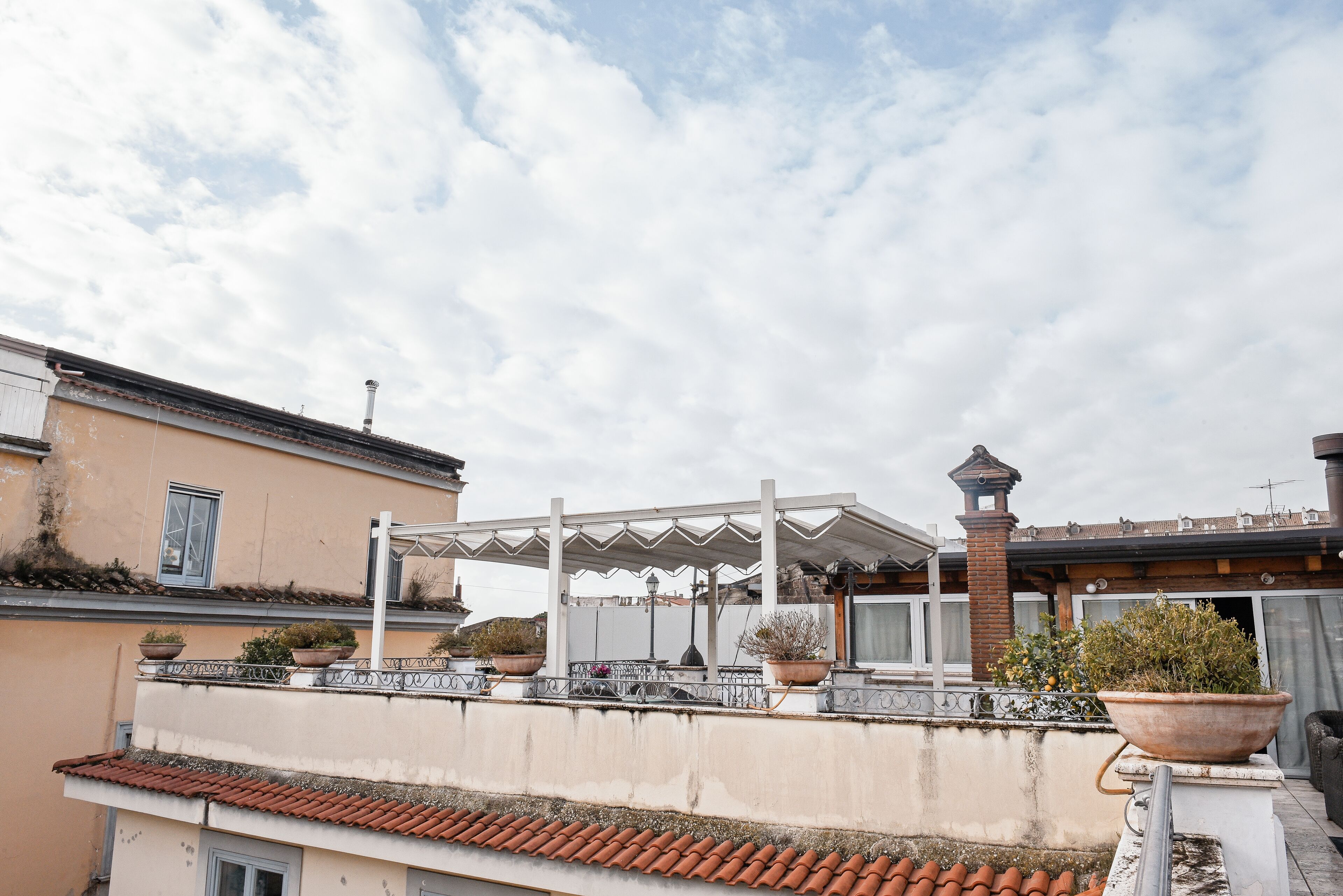 A rooftop terrace with a pergola, potted plants, and a view of the surrounding buildings.