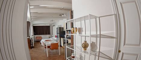 A spacious room with a dining area, a kitchen, and a white door with a decorative vase.