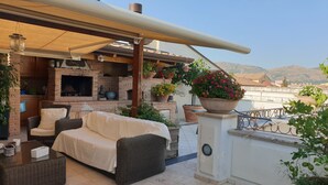 Una terraza en la azotea con mobiliario exterior, una chimenea de ladrillo y plantas en macetas.