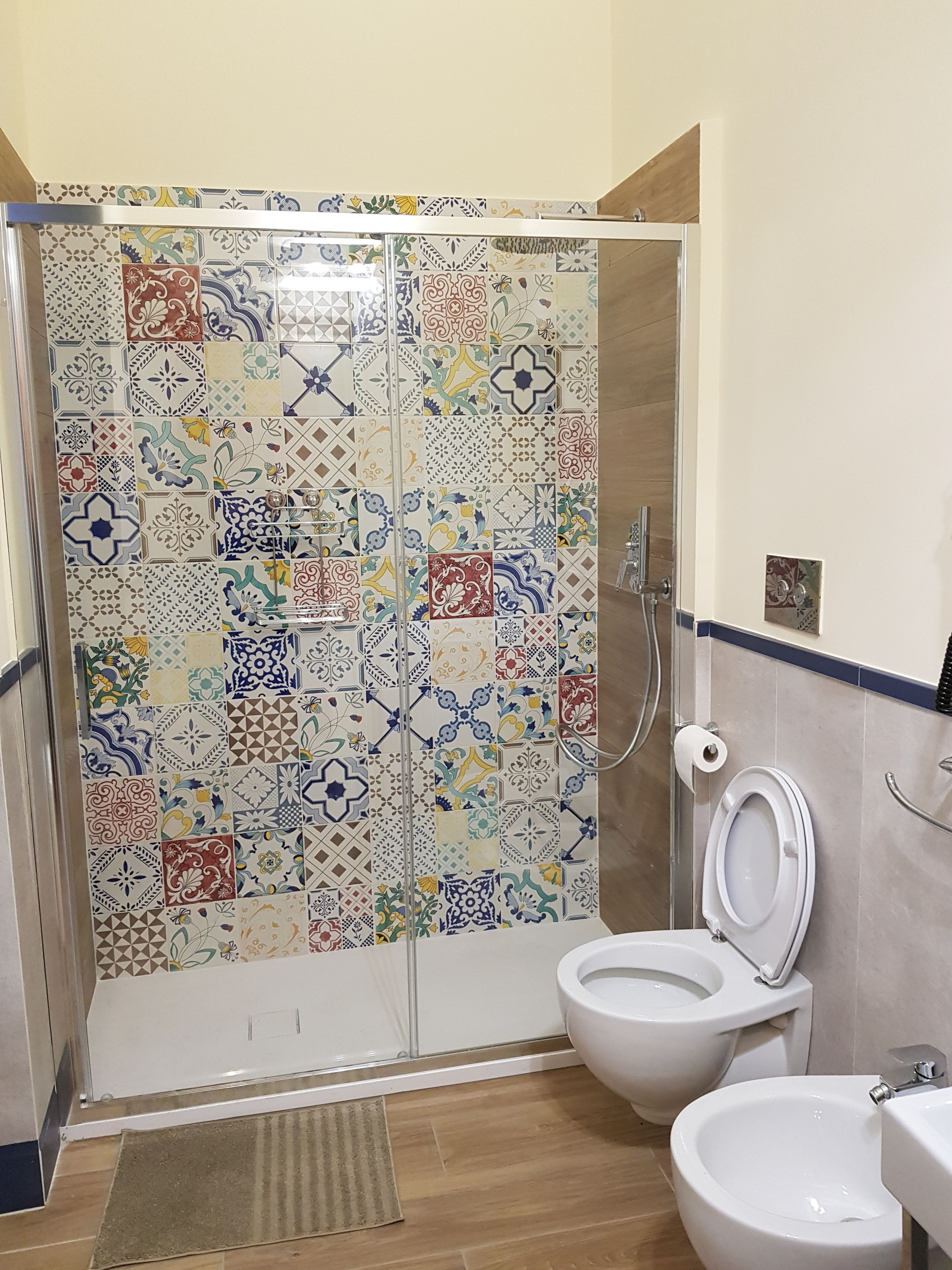 A bathroom with a shower enclosure tiled with a variety of patterns, a toilet, and a bidet.
