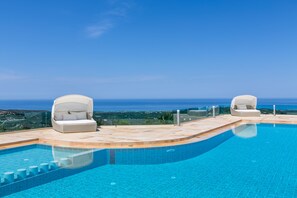 Una piscina con dos sillas blancas acolchadas y vista despejada al océano.