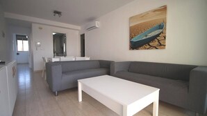 Una sala de estar moderna con un sofá gris, una mesa de centro blanca y un cuadro de un barco en la playa.
