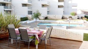 Un espacio de comedor al aire libre con piscina y un edificio blanco al fondo.