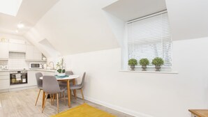 A modern kitchen with white cabinetry, a dining table with chairs, and a yellow rug. - 1 Bedroom City Centre Holiday home (York)