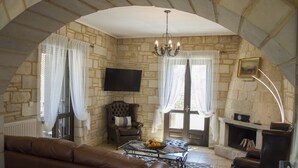Une pièce aux murs de pierre, dotée d’une cheminée, d’un téléviseur, d’un canapé et d’une table basse sur laquelle sont disposés des fruits.