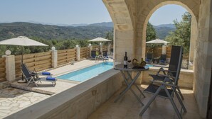 Un espace aménagé au bord de la piscine, offrant une vue sur les montagnes, avec des murs en pierre et des sièges d’extérieur.