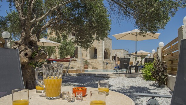 Un espace de restauration en plein air, aménagé avec des tables, des chaises et des parasols, entouré d’arbres et bordé d’une piscine.