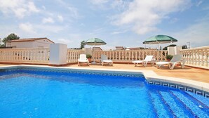 A swimming pool with clear blue water, surrounded by white lounge chairs and green umbrellas. - Olivia: Villa with private pool in L'Escala (L'Escala)