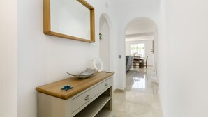Un pasillo con una consola de madera, un espejo y un cuenco. En el fondo, se ve una zona de comedor con una mesa y sillas.