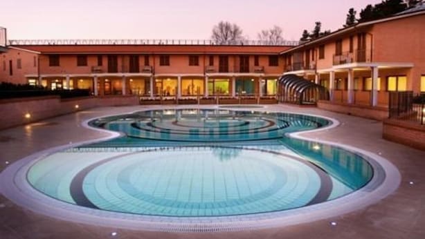 A hotel with a large, circular swimming pool in the center, surrounded by multiple-story buildings with balconies. - Hotel Eden Spa (Sarnano)