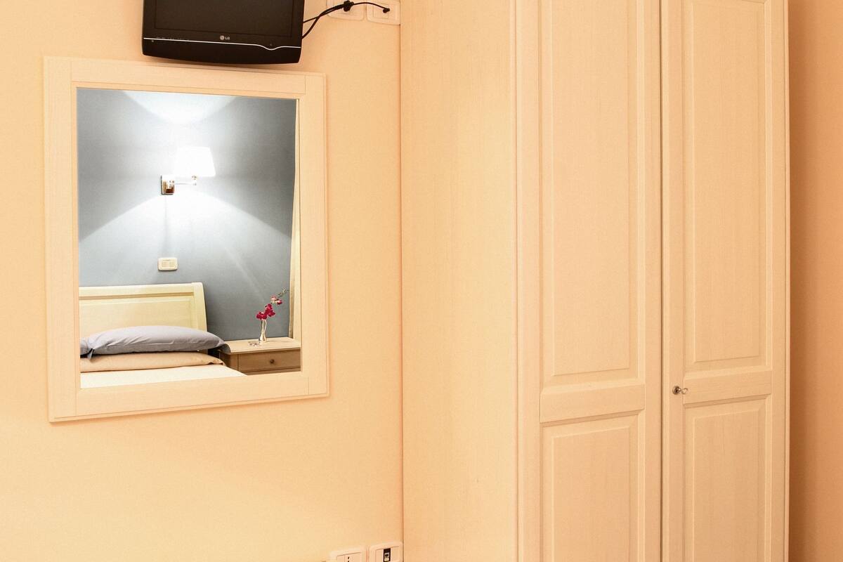 A bedroom with a bed, bedside table, mirror, wardrobe, and a television mounted on the wall.