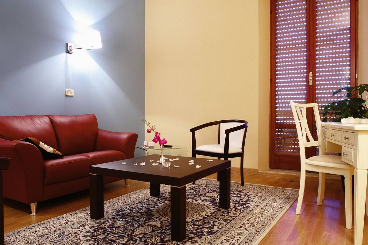 A living room with a red leather sofa, a wooden coffee table, a white chair, and a desk with drawers.