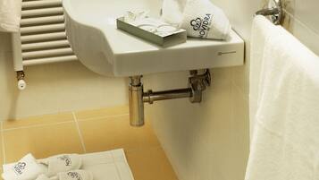 Ein Badezimmer mit Waschbecken, Spiegel und Handtuchhalter. Auf dem Boden liegen Hausschuhe und Toilettenartikel.