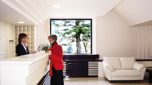 A reception area with a counter, a white sofa, and a large window with a tree view. - Hotel Eden Spa (Sarnano)