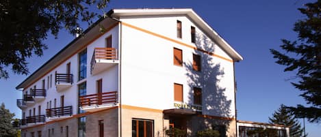 Un hotel de varios pisos con fachada blanca y detalles naranja, y balcones.