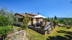 Ein Haus mit Steinmauer, einer überdachten Terrasse und Blick ins Grüne.