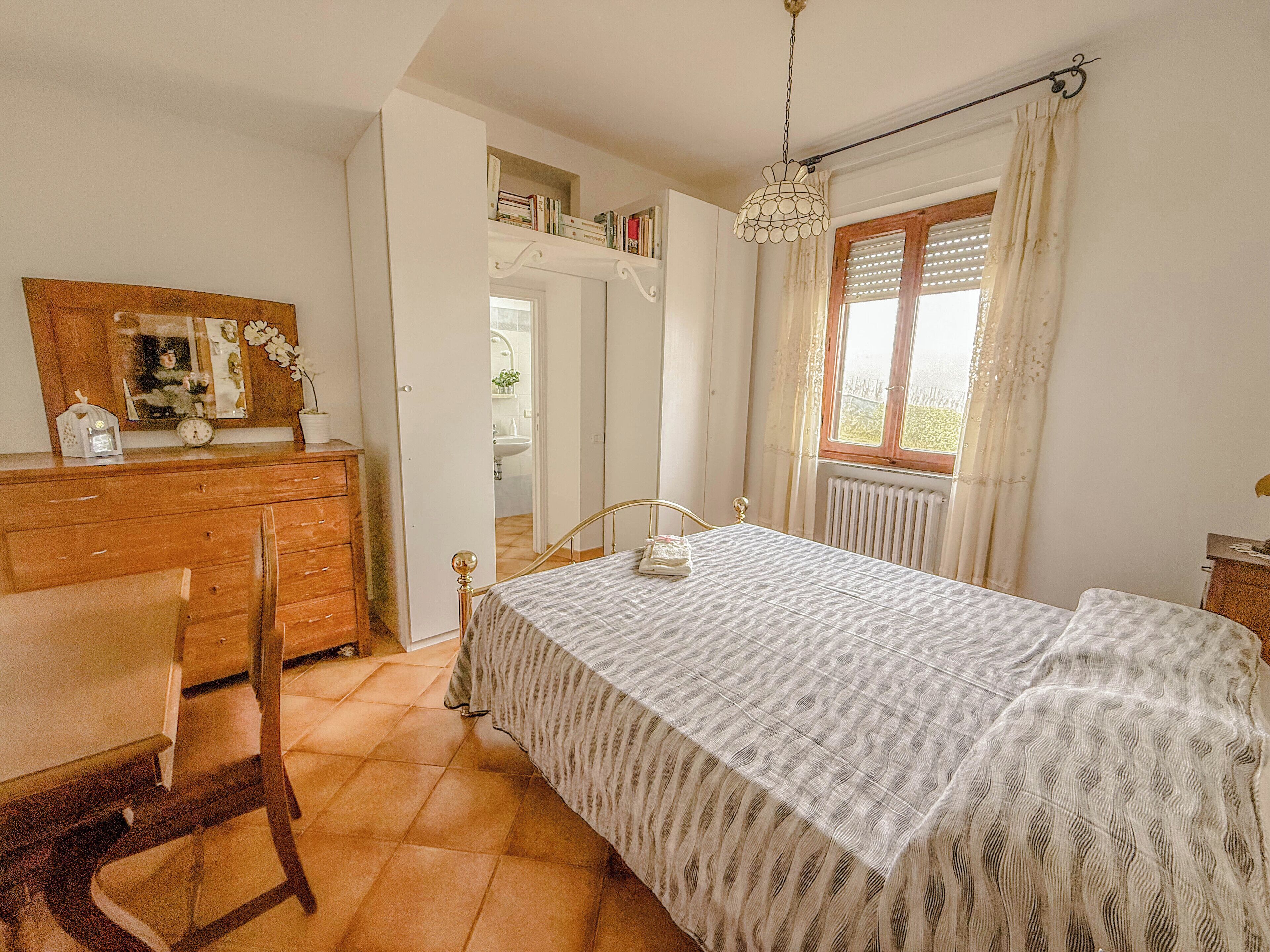 Ein Schlafzimmer mit Bett, Holzkommode, Stuhl und einem Fenster mit Vorhängen.