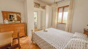 Ein Schlafzimmer mit Bett, Holzkommode, Stuhl und einem Fenster mit Vorhängen.