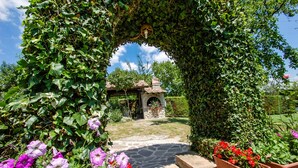 Ein Garten mit einem Kiesweg, der zu einem Gazebo führt, umgeben von üppiger Vegetation und blühenden Pflanzen.